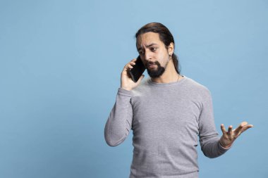 Saldırgan genç adam bir telefon görüşmesi sırasında sinirlenip sinirleniyor, çığlık atıyor ve mavi arka plana karşı öfkeli hissediyor. Erkek kişi kötü haberden rahatsız oluyor ve rahatsız oluyor..