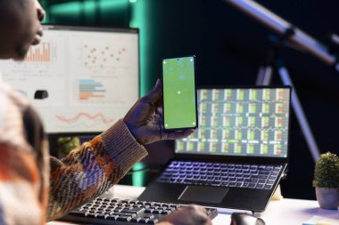 Afrikalı Amerikalı danışman masasının yanındaki yeşil ekranda muhasebe analizi için sermaye fonu istatistiklerini inceliyor. Banka uzmanı şirket bütçesini değerlendiriyor..