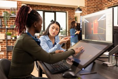 Siyahi kadın çalışan, Asyalı kreatif yöneticisine projedeki son gelişmeleri bildiriyor. Profesyonel kadın editörler başlangıç tasarımında işbirliği yapıyor, tuğla duvar ofisindeki fikirleri paylaşıyorlar.