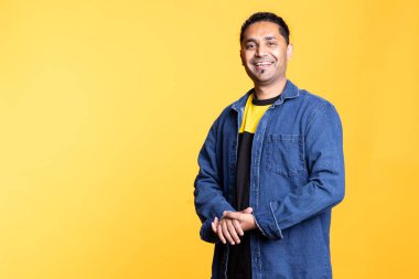 Gülümseyen ve kollarını kavuşturup stüdyonun arka planında duran neşeli Hintli adamın portresi. Neşeli, neşeli erkek kıyafetleri içinde olumlu duygular sergiliyor..