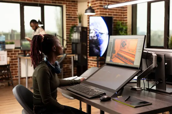 Siyahi kadın editör ofis masasında oturmuş dijital monitörlerine bakıyor ve projesini gözden geçiriyordu. Kulaklıklı Afrikalı Amerikalı kadın montajlanmış videolarını inceliyor..