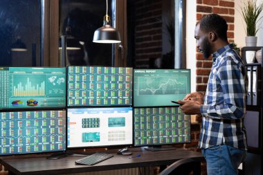 Modern bir ofisteki çoklu ekran kurulumu için tablet kullanan ve önx pazar eğilimlerini gözden geçiren bir finans analisti. Gece ayarı, dijital teknolojinin kullanımı ile yoğun çalışma verimliliğini vurguluyor.