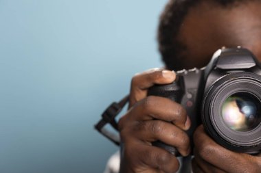 Stüdyoda mavi arka planı olan profesyonel bir kamera kullanan siyah bir erkek fotoğrafçı. Afrika kökenli bir Amerikalının DSLR 'ı nasıl kullanacağını göstermesine odaklan..