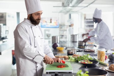 Üniformalı aşçı uzman aşçı fırında taze kesilmiş sebzeler hazırlıyor, kesme tahtasında dolmalık biber doğruyor. Aşçı, taze ürünlerle modern bir mutfakta çalışıyor..