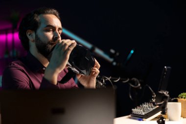 Seyircilere VR gözlüklerini sunan adam tripodla akıllı telefonuyla video çekiyor. Hayranlara önermeden önce sanal gerçeklik ürünü değerlendiren içerik yaratıcısı, cep telefonuyla çekim yapıyor