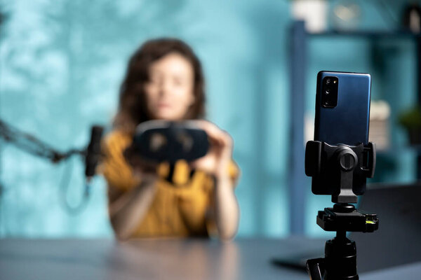 Сосредоточьтесь на смартфоне, используемом техническим блогером для просмотра VR очков в студии. Крупный план телефона, используемого женщиной для съемки видео презентации виртуальной реальности