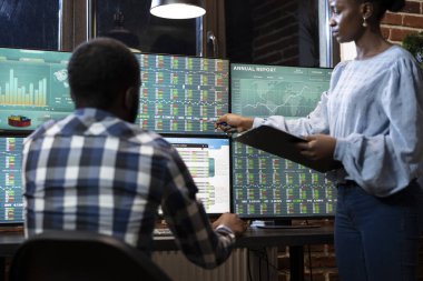 İki tüccar gece geç saatlere kadar modern bir ofiste çalışıyorlar, birden fazla monitörde işbirliği yapıyorlar, önx pazar grafikleri ve hisse senedi verileri gösteriyorlar. Afro-Amerikan iş ortakları hisse senedi ticaret verilerini inceliyor.