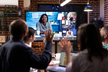 Çok ırklı bir girişim ekibi sanal toplantı sırasında pazarlama stratejilerini tartışıyor ve fikirlerini uzak meslektaşlarıyla paylaşıyor. İş arkadaşlarıyla video görüşmesi için dijital ekran kullanan çeşitli profesyoneller.