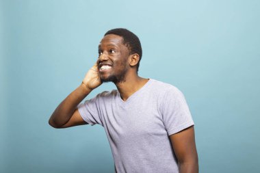 Gülümseyen Afro-Amerikan bir adam kulağını kavrıyor, sanki bir sohbeti yakalamaya çalışıyormuş gibi merakla eğiliyor. Neşeli siyah erkek birey dikkatle dinliyor, büyük bir ilgi gösteriyor ve odaklanıyor..