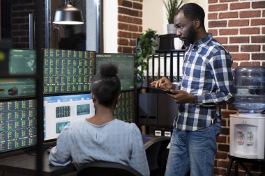 Geç saatlere kadar çalışan iki borsacıdan oluşan bir Afro-Amerikan ekibi. Forx çizelgelerini ve tuğla duvar ofisindeki birden fazla monitörün mali verilerini inceliyorlar. Tabletli bir erkek müdür iş arkadaşıyla işbirliği yapıyor..