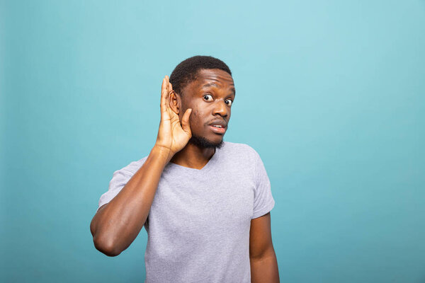 Афроамериканец прижимает ухо, чтобы лучше слышать, выражая любопытство и интерес. Портрет черного мужчины, слушающего внимательно, подслушивающего разговор.