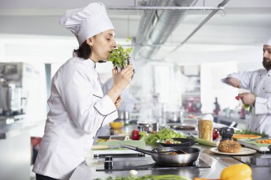 Kendini adamış kadın şef taze biberiye ya da maydanoz yaprakları kullanarak ve tavaya serpiştirerek otların ve yeşilliğin kokusunu kokluyor. Mutfak uzmanı hammadde ve gastronomiyle yemek pişiriyor..
