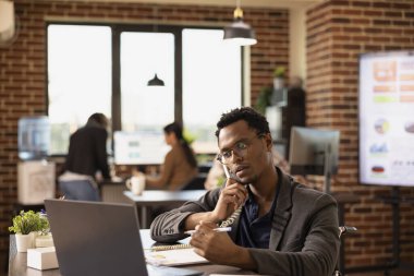 Elinde kalemle Afrikalı Amerikalı bir çalışan bir müşteriye iş büyümesi hakkında bilgi veriyor. Tekerlekli sandalyedeki siyah adam şirket araştırma verilerini incelerken sabit telefon kullanıyor..