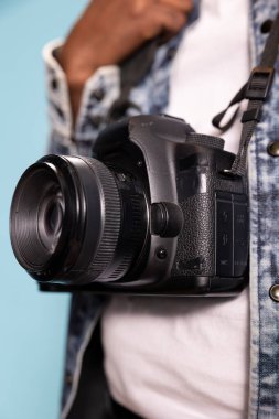 Gayri resmi kıyafette siyah bir şahsın taktığı kameraya odaklanın. Cihazın tasarımını vurgulayın. Beyaz gömlek ve kot ceketin üzerinde asılı DSLR yakın plan, fotoğrafçılık teçhizat ayrıntıları üzerinde.