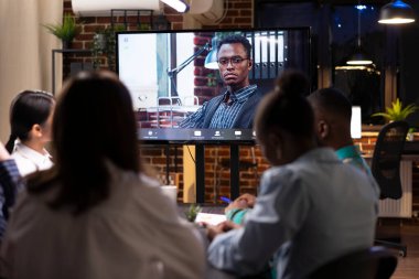 İş adamı iş arkadaşlarıyla sanal görüşmede dijital monitörde. Siyah erkek girişimci, video konferans çağrısı sırasında pazarlama stratejileri üzerine beyin fırtınası oturumuna katkıda bulunuyor..