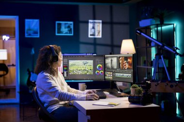 Video editörü, film kurgusunu analiz ediyor. Ev stüdyosundaki renk dengesi ve ışıklandırmayı düzenlemeden önce. Yapım stüdyosu çalışanı kulaklıkla şarkılar dinlerken ham görüntülerle çalışıyor.