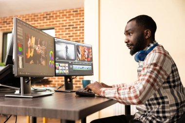 Kulaklıklı siyah erkek editör, bilgisayar ekranlarındaki dijital görüntülerin kalitesini arttırıyor. Afrika kökenli Amerikalı prodüksiyon uzmanı film çerçevelerini rafine etmek için çoklu monitör düzeneği kullanıyor.