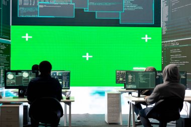 Siber güvenlik uzmanları, bir devlet dairesinde şifreleme ve bilişim güvenliği kullanarak büyük bir ekranda modelleme planı üzerinde çalışıyorlar. Rakip devlet sistemlerini hacklemek için siber operasyonlara odaklanılıyor.