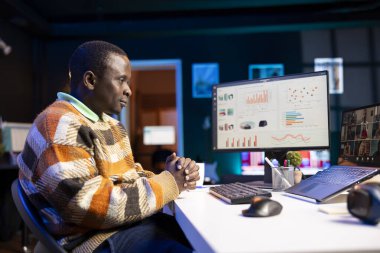 Siyahi adam görüntülü arama yapıyor ve iş bilgileri hakkında konuşuyor, aylık bütçe bakiyesini gözden geçiriyor ve uzaktan çalışıyor. Personel, bilgisayarda yapılan çevrimiçi toplantı sırasında konuşmaya odaklandı.