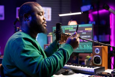 Sanatçı söz yazarı, yeni müzikal eserini akustik versiyon tanıtımı için yeni bir şarkı kaydederek ev stüdyosunda sahneleyecek. Genç besteci melodik öğeleri ve mısraları okumak için telefon kullanır.