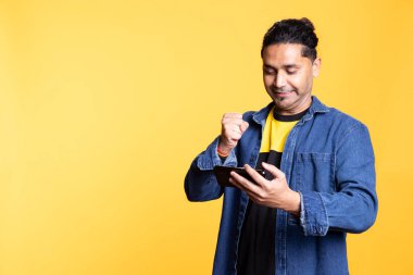 Oyun konsolunda oyun kazandıktan sonra stüdyo arka planında ayakta duran mutlu oyuncu kutlaması. Video oyunu müsabakasında zafer kazandıktan sonra övünen Hintli adam düşmanlarını yendi..