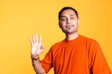 Çok mutlu bir adamın portresi turuncu arka planda birine el sallıyor, insanları selamlıyor ve gülümsemesini kamerada gösteriyor. Neşeli, dost canlısı Hintli adam stüdyoda çok mutlu..