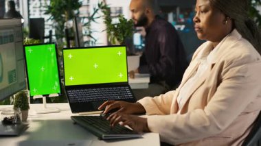 Ofis masasında bilgisayardaki belgeleri düzenleyen çalışanın yanında izole ekran bilgisayarı ve tablet var. Veri tablolarını analiz eden, istatistiksel bilgileri yorumlayan, kamera A 'nın yanındaki krom anahtar aygıtlar