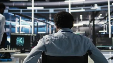 Paraplejik sunucu odası programcısı yapay zeka veri analizi grafiklerini yorumluyor. Tekerlekli sandalyedeki adam yapay zeka programı kullanarak veri merkezinde, kamera A 'da öngörü ölçümleri gösteriyor.
