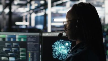 Veri Merkezi çalışanı, bildirilen sorunları gidermek için ses kulaklığı ve görsel programlama paneli kullanıyor. Sunucu çiftliği teknisyeni düğüm ağacı arayüzüne bakıyor, mikrofonla konuşuyor