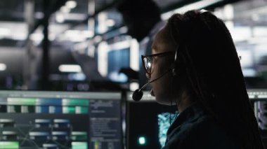 Veri merkezi uzmanı düğüm ağacı arayüzünü inceleyerek teknik destek sağlıyor. Sunucu odası teknisyeni iş arkadaşlarıyla mikrofonla konuşuyor, görsel programlama yazılımı kullanıyor, kamera B