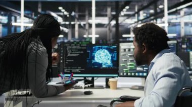 Tekerlekli sandalyedeki veri merkezi mühendisi ve meslektaşı düğüm ağacı programlama aracı kullanarak otomatik görevleri denetliyor. Özel sunucu tarım ekibi, AI analizlerine ve kamera A 'ya dayalı sistem ayarlarını ayarlar