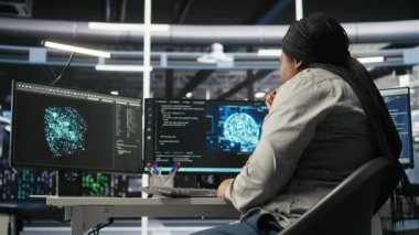 Veri merkezi teknisyeni donanımı yapılandırmak için yapay zeka derin öğrenme modelleri kullanıyor. Afro-Amerikalı kadın sunucu odasında yapay zeka programlama dili üzerinde çalışıyor, sistemi optimize ediyor, kamera A