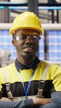 Güneş paneli üretim ekipmanlarını denetleyen teknisyenlerin dikey video portresi. Otomatik endüstri 4.0 fabrikasında bilgisayar kullanarak fotovoltaik montaj sistemlerini sürdüren Afrikalı Amerikalı bir adam.