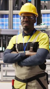 Güneş paneli üretim ekipmanlarını denetleyen teknisyenlerin dikey video portresi. Otomatik endüstri 4.0 fabrikasında bilgisayar kullanarak fotovoltaik montaj sistemlerini sürdüren Afrikalı Amerikalı bir adam.