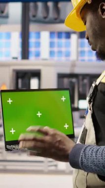 Dikey video mühendisi yeşil ekran dizüstü bilgisayar kullanarak güneş paneli üretim hatları ekipmanlarını denetliyor. İşçi otomatikleştirilmiş sanayi 4.0 fabrikasında krom anahtar kullanarak fotovoltaik montaj sistemleri sürdürüyor