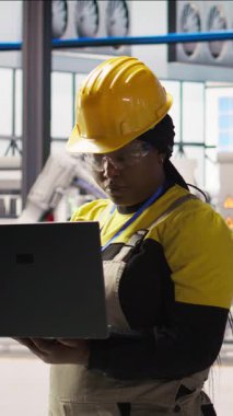 Gülümseyen güneş panelleri fabrika mühendisinin dikey video portresi dizüstü bilgisayardaki verileri analiz ederek vites arızalarını öngörüyor. Mutlu fotovoltaik fabrikası çalışanı, bakım prosedürlerini takip eden bir defter kullanıyor.