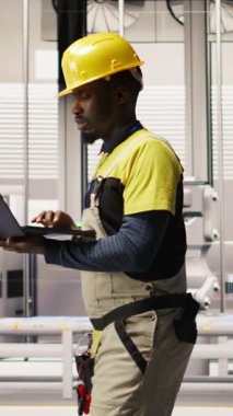 Dikey video mühendisi dizüstü bilgisayar kullanarak güneş paneli üretim hatlarını inceliyor, ekipman performansını analiz ediyor, otomatikman çevre dostu fabrikada fotovoltaik montaj sistemleri sürdürüyor, kamera A