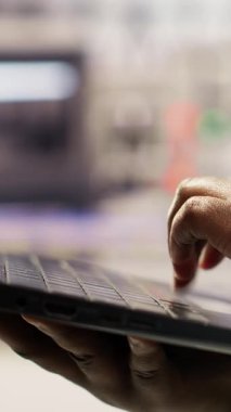 Dikey video endüstriyel fabrika uzmanı dizüstü bilgisayar ve sorun giderme hatalarını kullanarak kurulum sürecini denetliyor. İmalat tesisi çalışanı otomatik robotik silahları not defteri, kamera B kullanarak ayarlıyor.