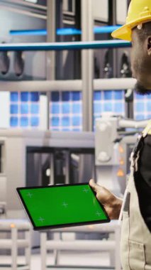 Akıllı fabrikadaki dikey video mühendisi yeşil ekran tableti kullanarak kalite kontrolü sağlayan robot montaj hatlarını denetliyor. İşçi krom anahtar aygıtı kullanarak otomatik taşıyıcı sistemlerini izliyor