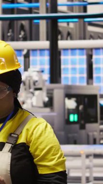 Güneş panellerinde çalışan dikey video kadın makine sistemlerini denetlemek için tablet kullanıyor. Afrika kökenli Amerikan fotovoltaik fabrikası çalışanı işlemleri sürdürmek için yazılımı kullanıyor, kamera A