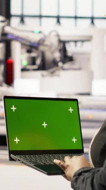 Endüstriyel fabrikadaki dikey video teknisyeni ekipman hatalarını teşhis etmek için yeşil ekran laptop kullanıyor. Montaj hatlarındaki tamir görevlerini koordine etmek için krom anahtar model dizüstü bilgisayar kullanan bir fabrika uzmanı