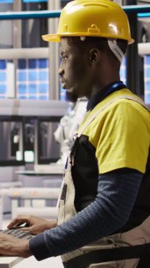 Dikey video akıllı fabrika çalışanı bilgisayar klavyesinde daktilo kullanıyor, otomatik sistemleri test ediyor, bakım yapıyor. Endüstri 4.0 fabrika çalışanı, bilgisayar kullanarak ekipmanları denetliyor ve hataları onarıyor, kamera A