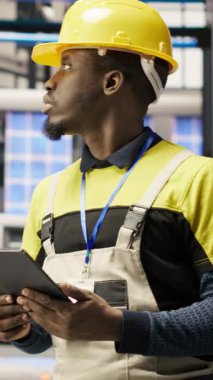 Teçhizatı değiştirmeden önce IoT sensörlerini analiz etmek için tablet kullanan dikey video akıllı fabrika teknisyeni. Endüstri 4.0 'daki Afrikalı Amerikalı adam dinlenme süresini azaltmak için sistem kontrolü yapıyor.