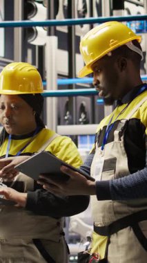 Akıllı fabrika mekaniklerinden oluşan dikey video ekibi sistemleri test etmek ve bakım yapmak için birlikte çalışıyor. Endüstri 4.0 fabrika ekip tamircisi. Arızaları tespit etmek için ekipmanları denetliyor.