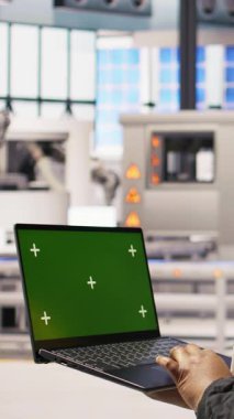 Dikey video fabrikası mühendisi yeşil ekran dizüstü bilgisayarda yazarak üretim hatlarını izliyor. Sektör 4.0 fabrikasındaki kadın, makinelerin krom anahtar modellemesi kullanarak en uygun verimlilikte çalışmasını sağlıyor.