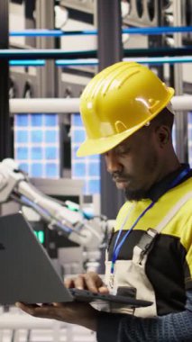 Güneş panelleri fabrikasındaki dikey video teknisyeni dizüstü bilgisayar kullanarak robot montaj hatlarını denetliyor ve kalite kontrolü sağlıyor. Endüstriyel fabrika işçisi otomatik taşıma sistemlerini not defteri kullanarak izliyor