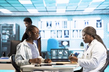 Rutin kontrol sırasında oksimetre kullanarak oksijen doygunluğunu ve nabız oranını ölçen bir sağlık uzmanı, modern tıbbi aletlerle siyah bir kıza danışın. Hayati belirtiler ölçümü.