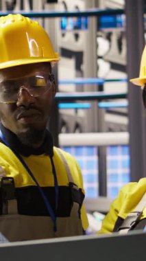 Dikey video güneş panelleri makine sistemlerini denetlemek için dizüstü bilgisayar kullanan bitki mühendisliği ekibi. Photovoltaics fabrikası çalışma arkadaşları, işlemleri sürdürmek için defter üzerinde yazılım kullanın, kamera A