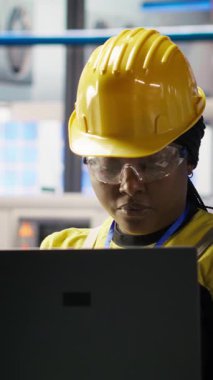 Gülümseyen güneş panelleri fabrika mühendisinin dikey video portresi dizüstü bilgisayardaki verileri analiz ederek vites arızalarını öngörüyor. Mutlu fotovoltaik fabrikası çalışanı, bakım prosedürlerini takip eden bir defter kullanıyor.