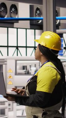Çevre dostu endüstriyel santraldeki dikey video teknisyeni defter kullanarak üretim ekipmanlarını izliyor ve arızaları teşhis ediyor. Fabrika çalışanı güneş panelleri montajındaki onarım görevlerini koordine ediyor